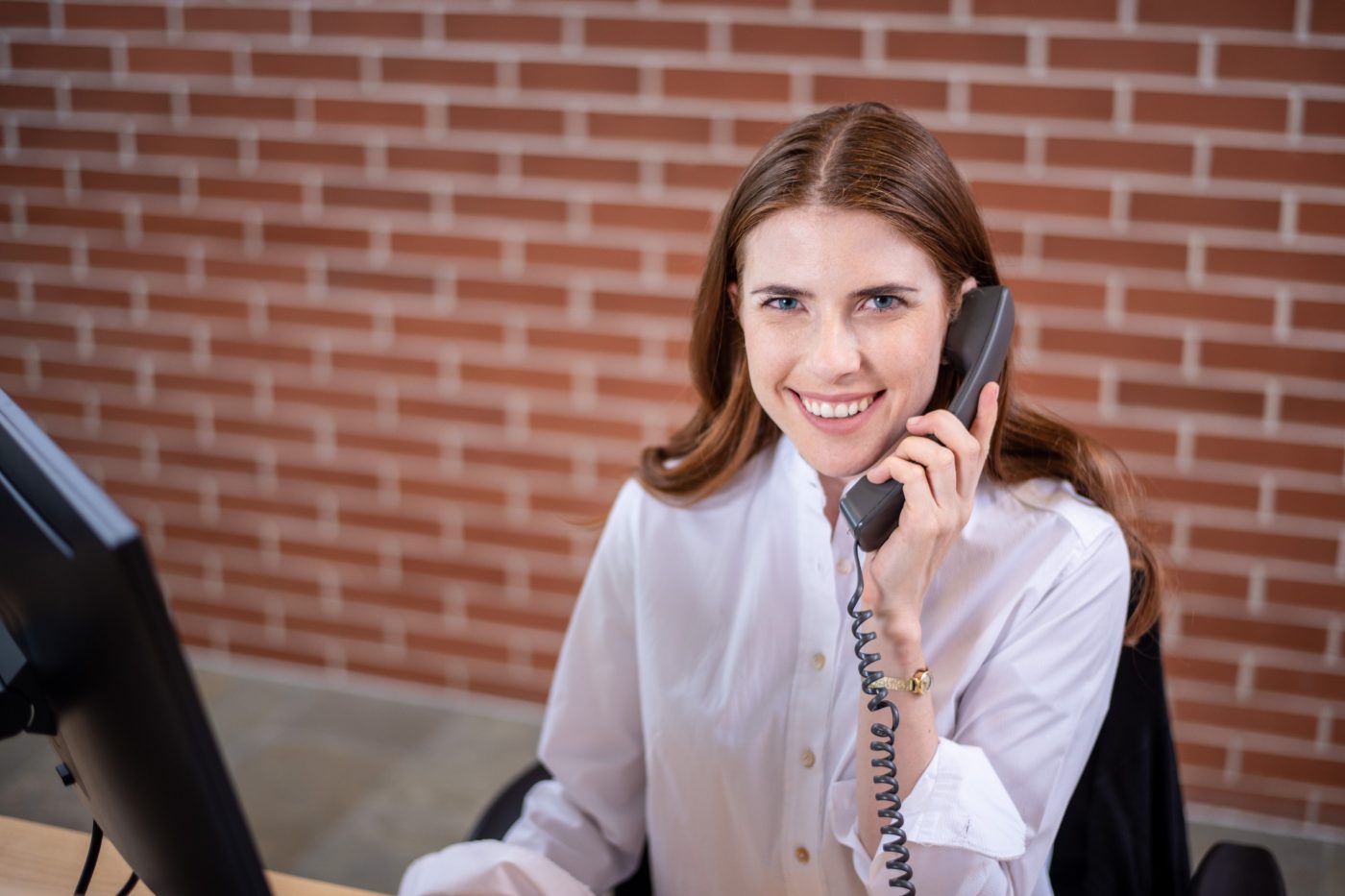 Smiling woman sitting next to computer screen holding a telephone receiver