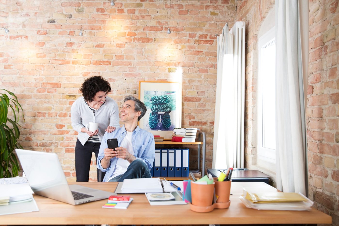 Man with phone in conversatuion with woman in front of brick-lined wall
