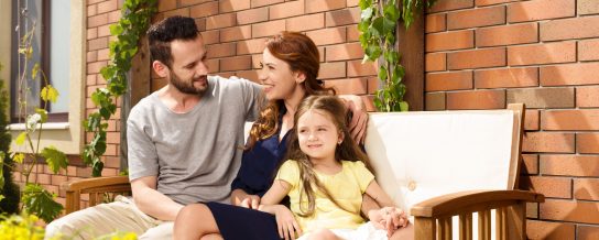 Young family sitting on garden bench in front of brick-lined façade