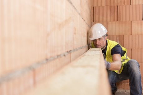 Construction worker checking alignment of mineral-wool filled clay block