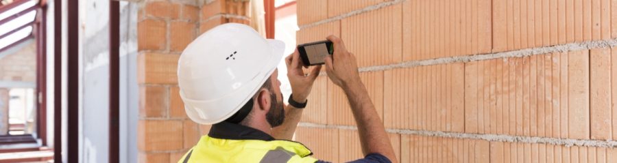 Builder whith saftey jacket and hard hat taking picture of bare brick wall