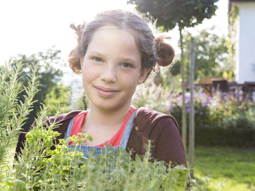 Girl with fresh herbs in garden facing camera