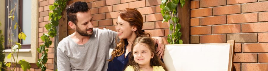 Young family sitting on garden bench in front of brick-lined façade