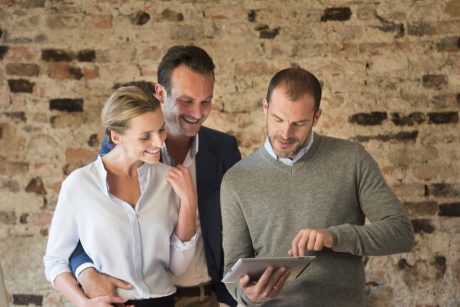 Architect presents project to couple in front of old brick wall on tablet 