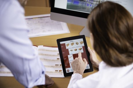 Woman at workplace holding tablet computer sitting next to standing man