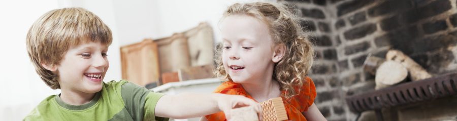 Boy and girl playing with miniature bricks, clay blocks and clay roof tiles in front of fireplace