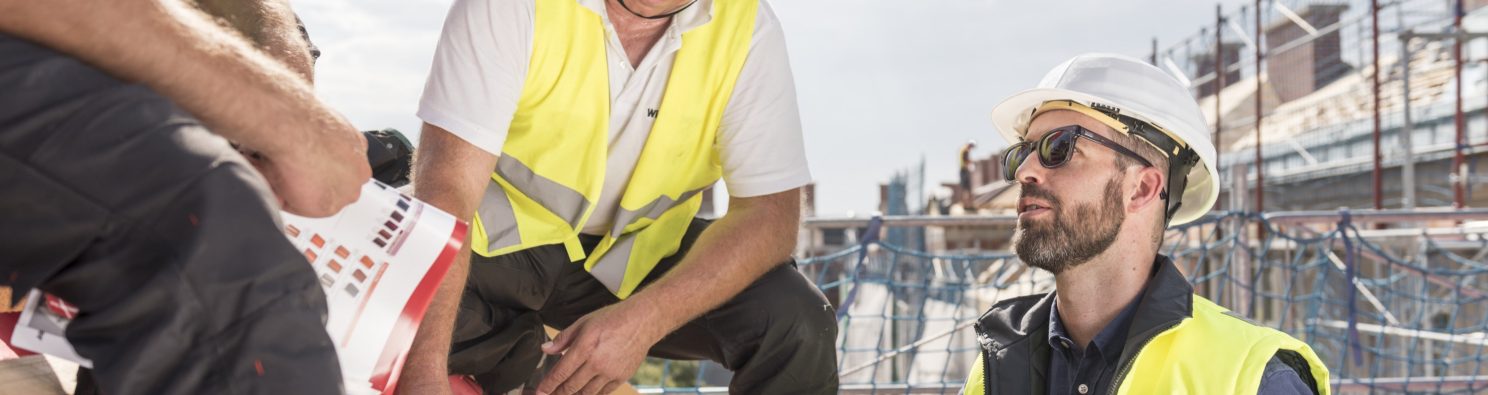 Product manager explaining product advantages to urban roofers wearing safety jackets and hard hats