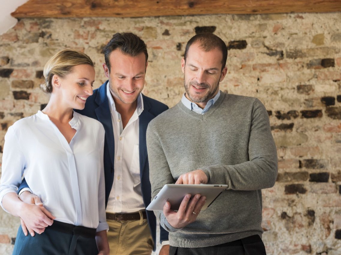 Architect presents project to couple on tablet in front of old brick wall 