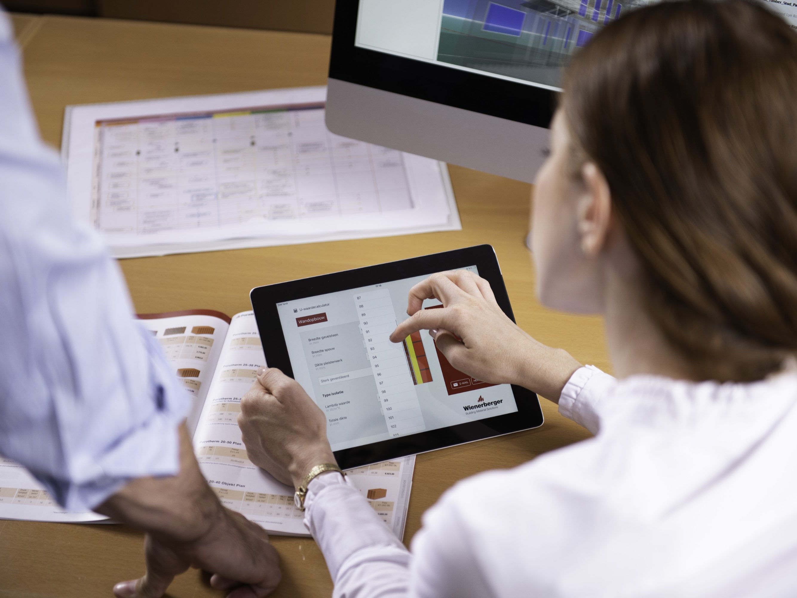 Woman at workplace holding tablet computer sitting next to standing man