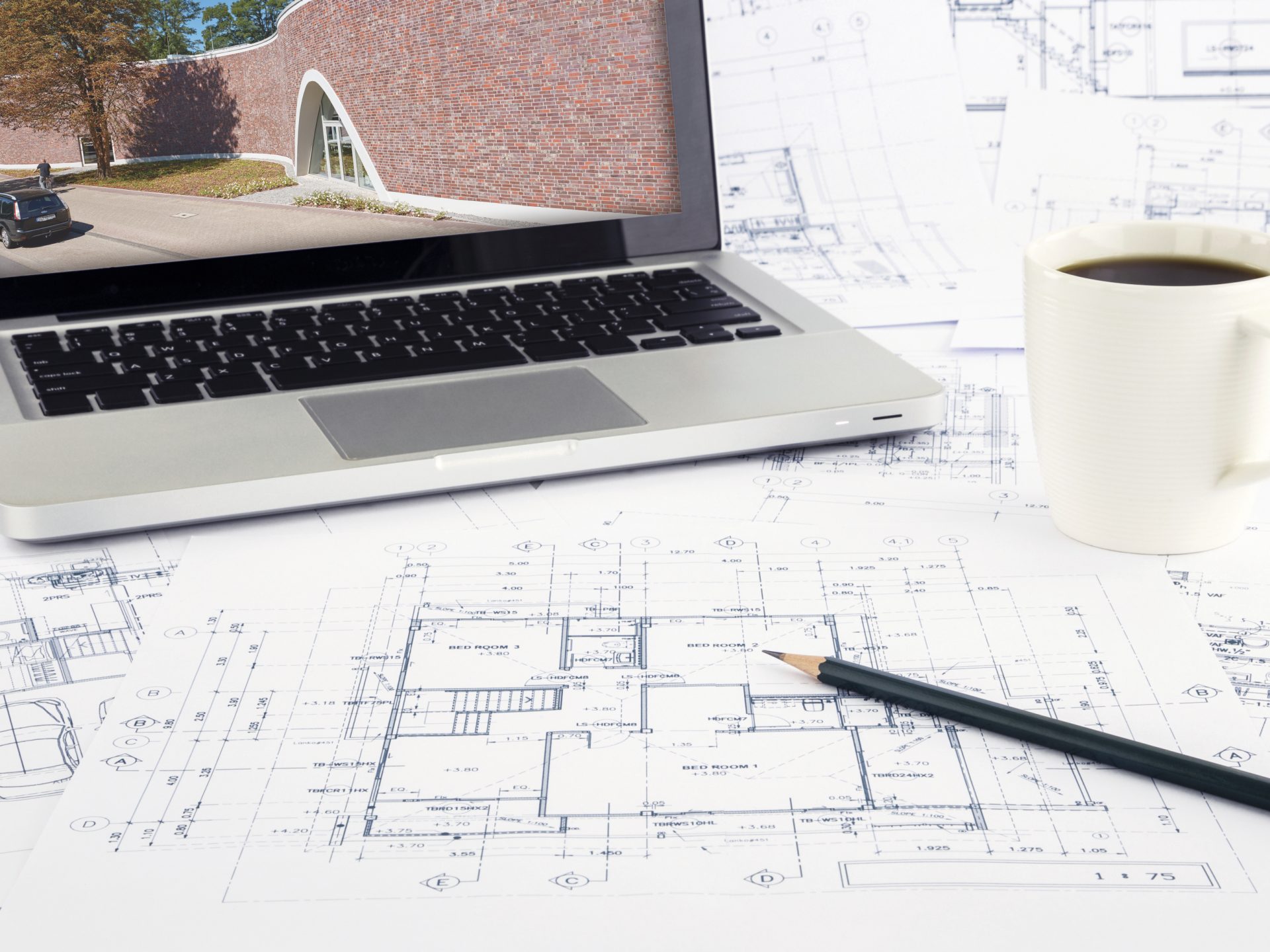 Working space with reference picture on laptop and architecture plan on desk