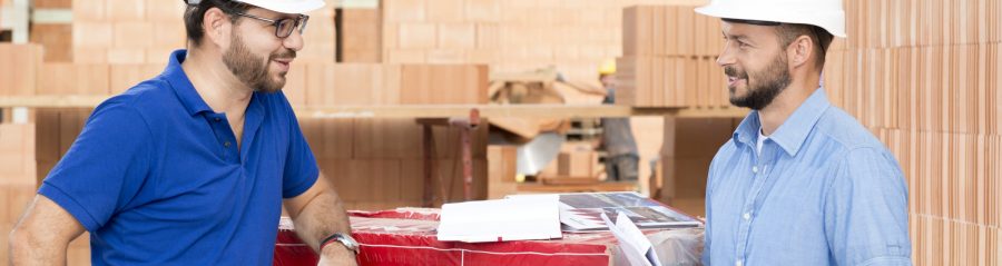 Building professionals talking at construction site next to foil wrapped pallette of brick blocks. > There is another version of this image available with another worker in the background