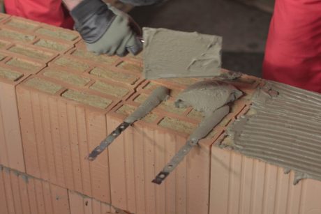 Hand of bricklayer laying with trowel mortar Porotherm Profi on the Porotherm bricks
