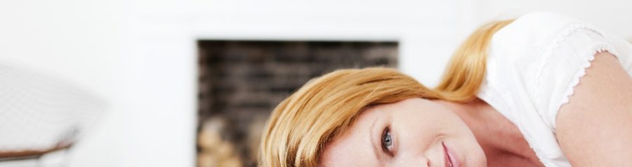 Woman lying on bed in front of brick-built fireplace facing camera
